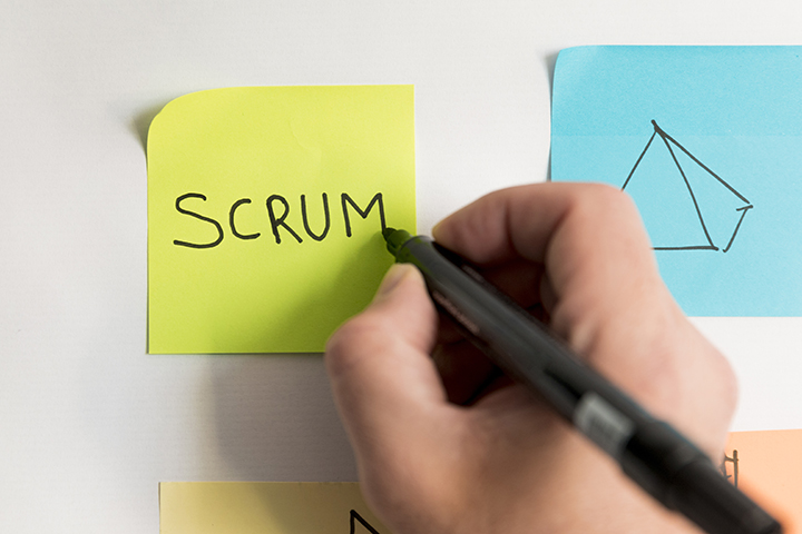 Mão escrevendo scrum em um postit