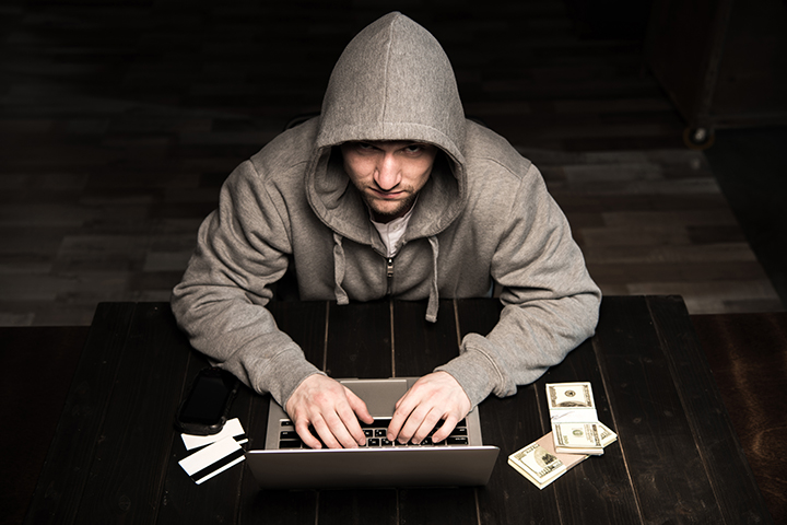 Jovem hacker com capuz sentado à mesa e usando laptop
