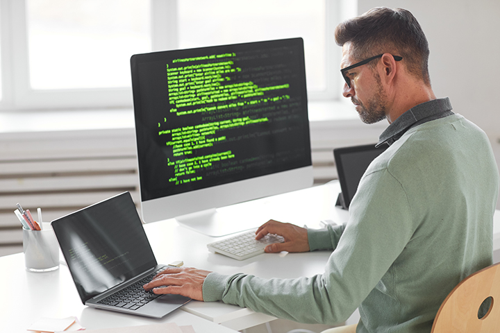 Homem usando desktop e o laptop para trabalhar e usando o PRINCE2