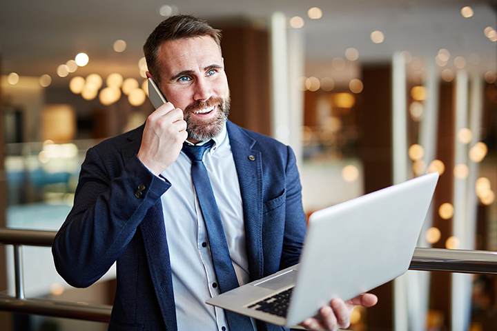 Homem gestor de TI falando ao telefone e segurando laptop