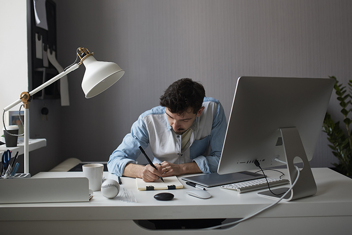 Homem fazendo anotações e trabalhando em desktop com projetos